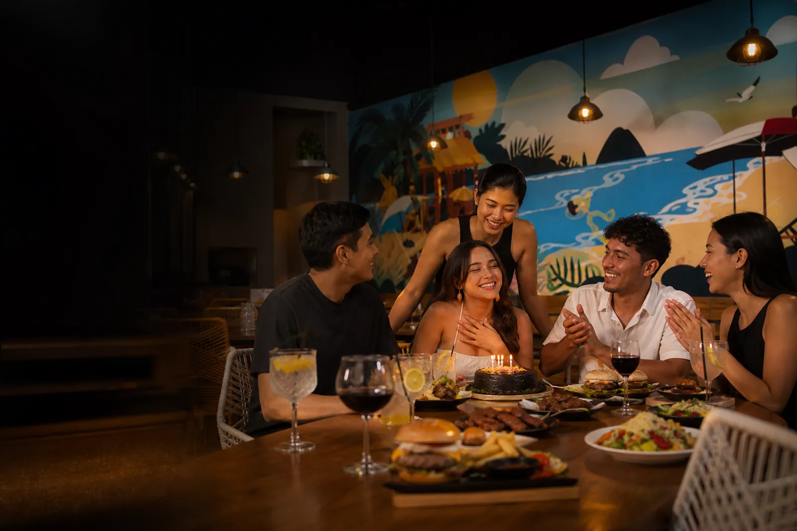 Grupo de amigos celebrando un cumpleaños con hamburguesas, cócteles y pastel en Ohana